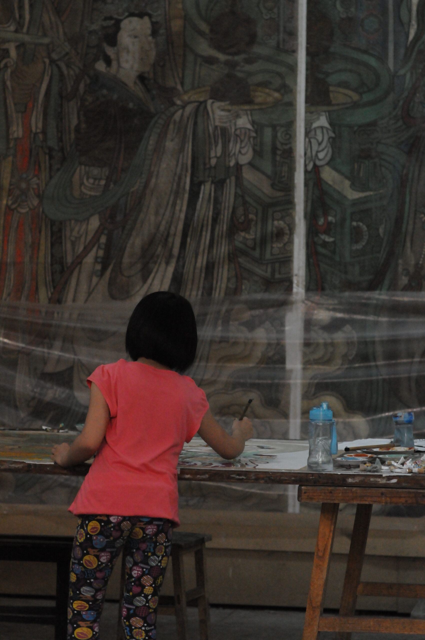 A child drawing in front of a mural